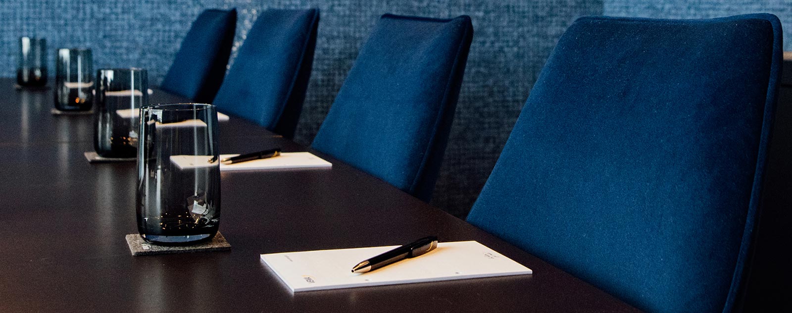 Ein Konferenztisch mit blauen Stühlen, Glaswasser und Schreibunterlagen.