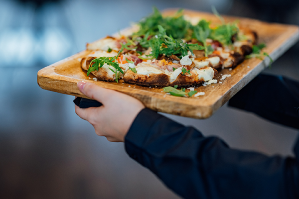 Galeriebild VEMA_0078.jpg Ein Holzbrett mit einer belegten Brotscheibe, garniert mit Rucola und Schinken.