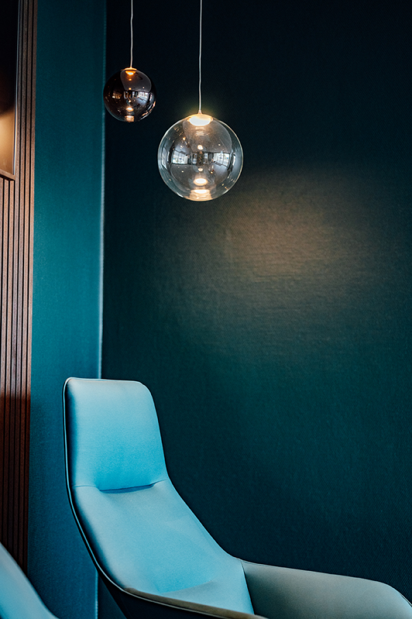 Galeriebild VEMA_0372.jpg Ein blauer Stuhl und zwei hängende Lampen vor einer dunkelblauen Wand.