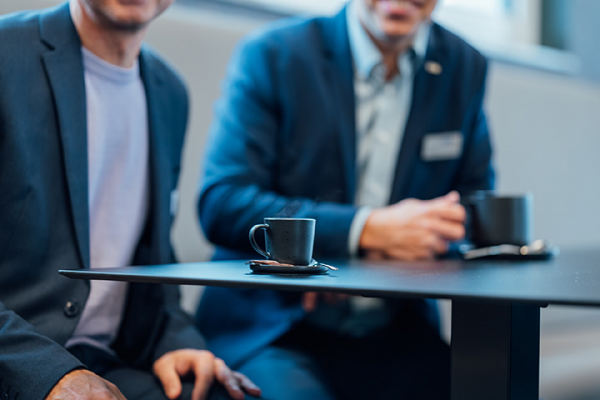 Galeriebild VEMA_0871.jpg Zwei Männer in Anzügen sitzen an einem Tisch mit Kaffeetassen.