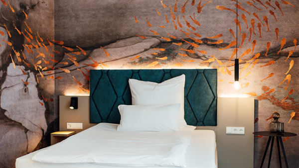 Galeriebild VEMA_2445.jpg Ein modernes Schlafzimmer mit einem blauen Kopfteil, weißen Kissen, einer künstlerischen Wand mit goldenen Fischen und einer Tischlampe.