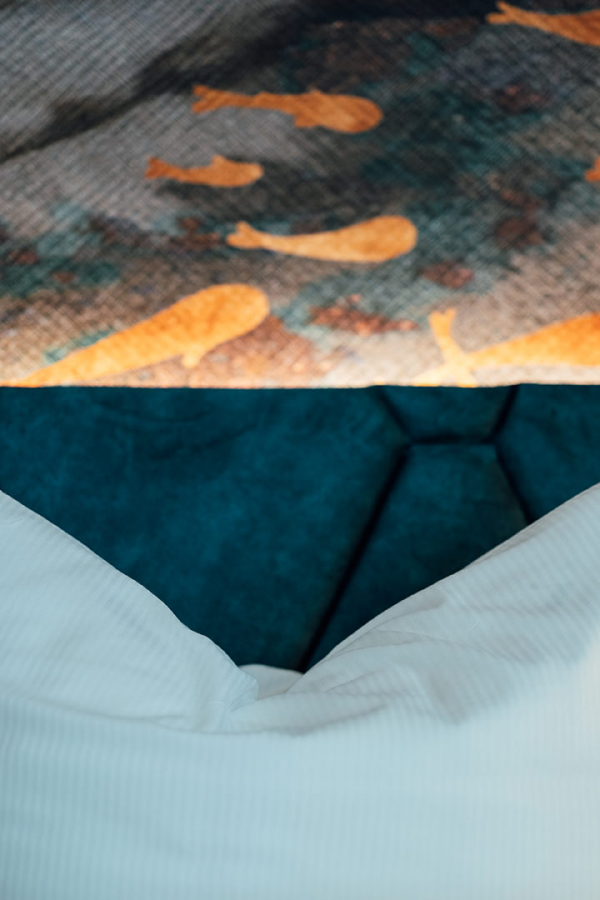 Galeriebild VEMA_2601.jpg Ein Bett mit weißen Kissen und einem Teppich mit Fischen in Warmtönen.