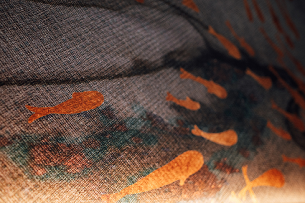 Galeriebild VEMA_2929-2.jpg Eine textile Oberfläche mit orangefarbenen Fischmotiven auf einem grauen Hintergrund.