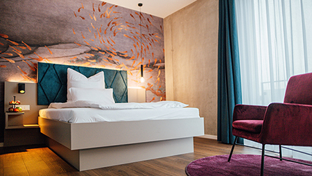 Galeriebild VEMA_2961.jpg Ein modernes Schlafzimmer mit einem großen Bett, einem Stuhl und dekorativer Wandgestaltung.