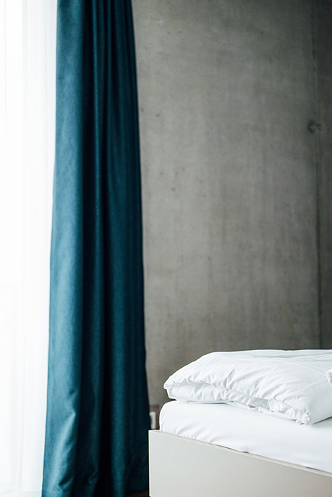 Galeriebild VEMA_3430.jpg Ein modernes Schlafzimmer mit einem Bett und einem blauen Vorhang vor einer Betonwand.