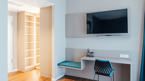 Galeriebild VEMA_3646_2.jpg Ein modernes Zimmer mit einem Fernseher, einem Tisch mit einem Stuhl und einem offenen Regal.