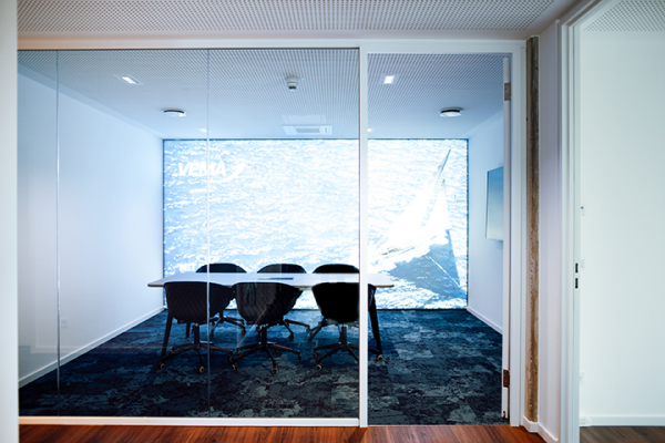 Galeriebild VEMA_4371.jpg Ein moderner Besprechungsraum mit Glaswänden und einem Bildschirm, der eine Segelboot- und Wasserlandschaft zeigt.