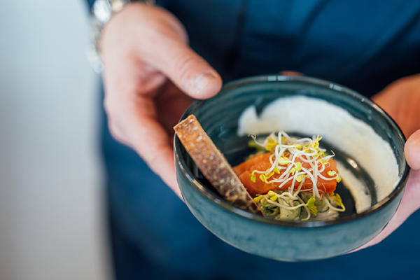 Galeriebild VEMA_4498.jpg Eine Person hält eine kleine Schüssel mit Lachs, Sprossen und einer cremigen Sauce.