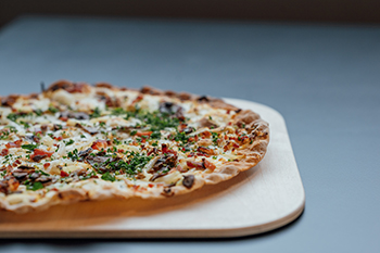 Galeriebild VEMA_5174A.jpg Eine frische Pizza mit Belägen auf einem Holzbrett.