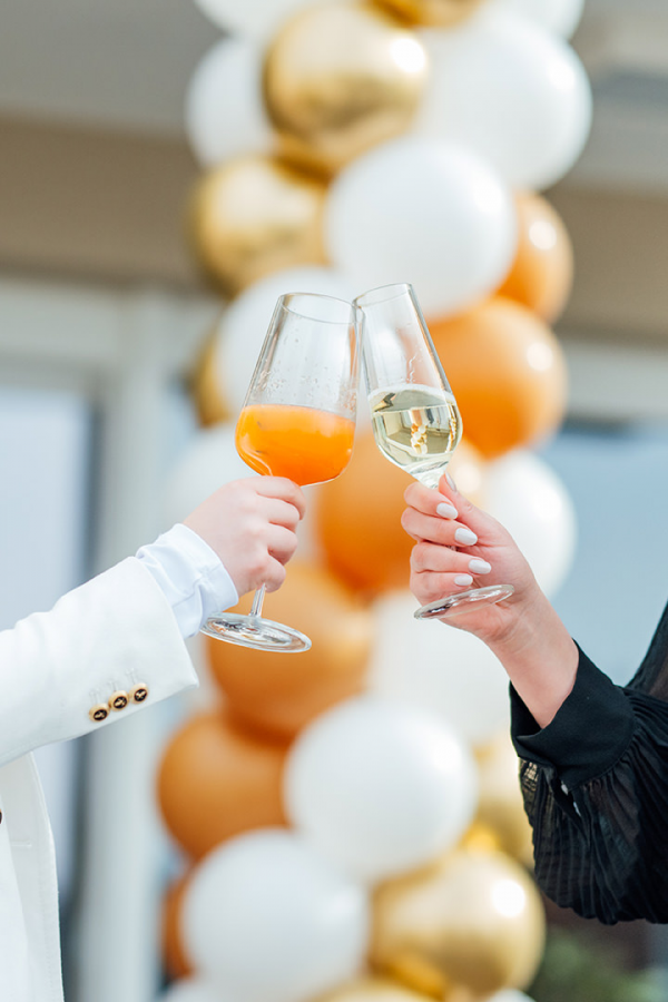 Galeriebild VEMA_5893.jpg Zwei Gläser mit Getränken werden angestoßen, im Hintergrund sind bunte Luftballons.