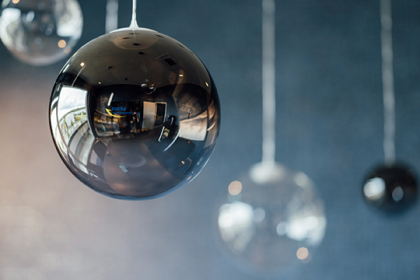 Galeriebild VEMA_6809.jpg Eine schwarze, glänzende Kugel hängt von der Decke, reflektiert Licht und die Umgebung. Weitere transparente und schwarze Kugeln sind im Hintergrund sichtbar.