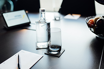 Galeriebild VEMA_6941.jpg Ein Tisch mit einer Glasflasche, einem Glas, einer Schreibunterlage und einer Schale mit Obst.