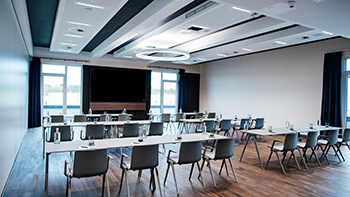 Galeriebild VEMA_7373.jpg Ein moderner Konferenzraum mit Tischen und Stühlen, Kreidetafel und viel natürlichem Licht.