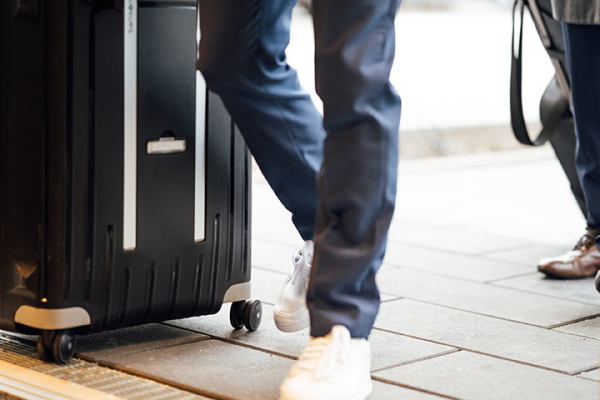 Galeriebild VEMA_8531.jpg Eine Person zieht einen schwarzen Koffer und trägt weiße Schuhe auf einem Gehweg.