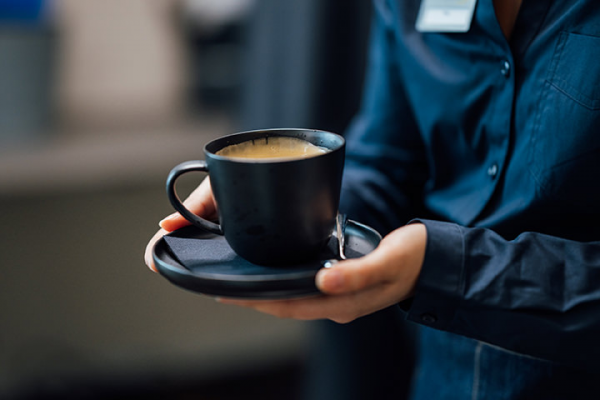 Galeriebild VEMA_8567.jpg Eine Person hält eine schwarze Tasse mit heißem Getränk auf einem Unterteller.