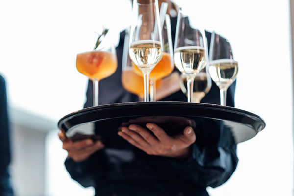 Galeriebild VEMA_8574.jpg Ein Kellner trägt ein Tablett mit verschiedenen Getränken, darunter Cocktails und Sektgläser.