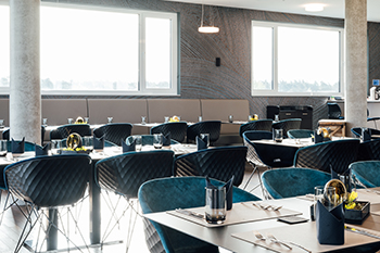 Galeriebild VEMA_8588.jpg Moderne Restaurant mit eleganten Tischen und Stühlen, großen Fenstern und einer stilvollen Einrichtung.
