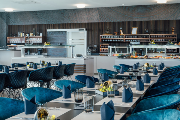 Galeriebild VEMA_8600.jpg Moderne Restaurantansicht mit blauen Stühlen, gedeckten Tischen und einem Buffetbereich.