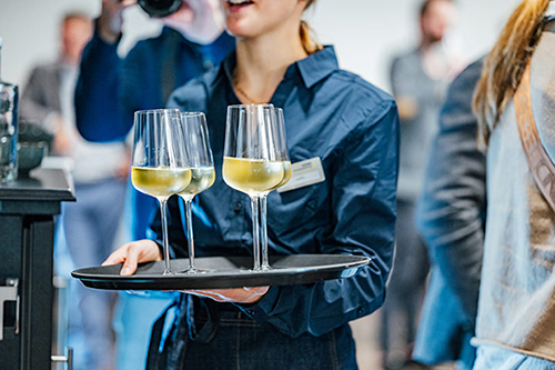Galeriebild VEMA_9401.jpg Eine Person trägt ein Tablett mit drei Gläsern Sekt.