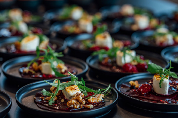 Galeriebild VEMA_9463.jpg Ein Teller mit einem Dessert, bestehend aus einer roten Sauce, Käsewürfeln, Nüssen und frischen Kräutern, präsentiert in mehreren identischen Portionen.