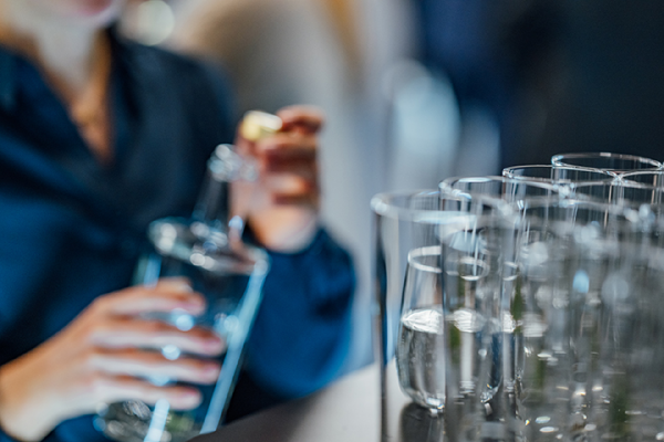 Galeriebild VEMA_9678.jpg Eine Person hält eine Flasche und füllt Gläser in der Nähe von einem Tisch mit mehreren Gläsern.